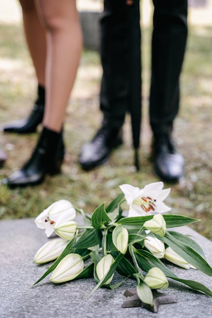 A bouquet of fresh white lilies and closed buds with long green leaves lies on the ground, with the stems and petals showing a smooth texture and delicate appearance. In the background, the blurred lo